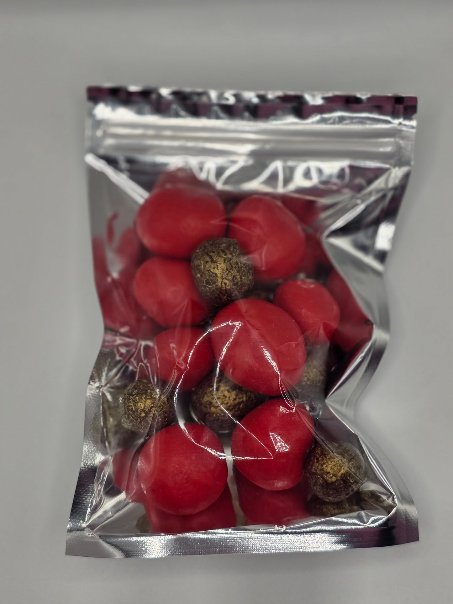 Coffee My Cup Sweet Treats Collection: Prosecco Berry Bliss – 4oz Bag: Red spherical objects with brown centers in a clear plastic bag on a gray background