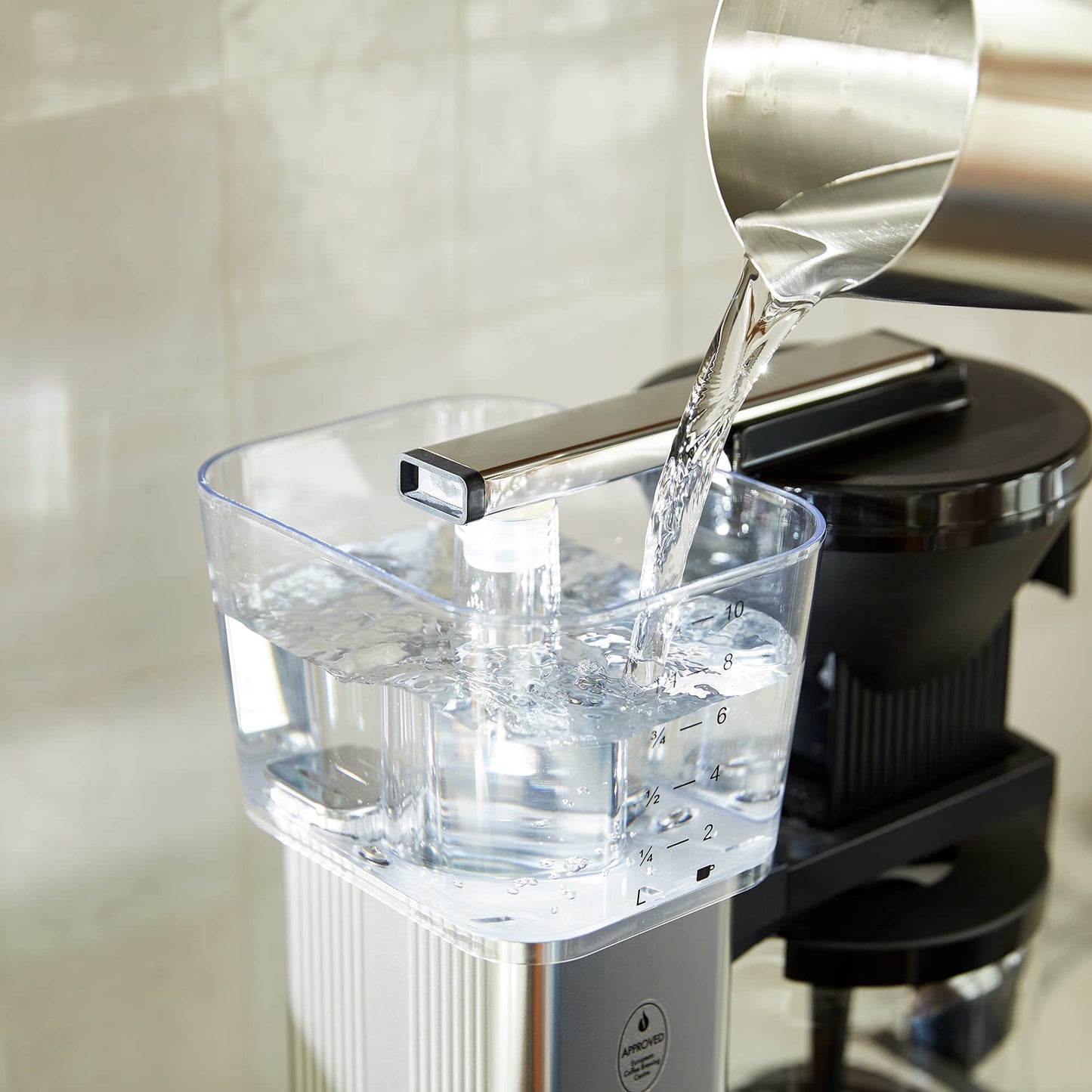 Clear container being filled with water from a faucet on a kitchen counter.